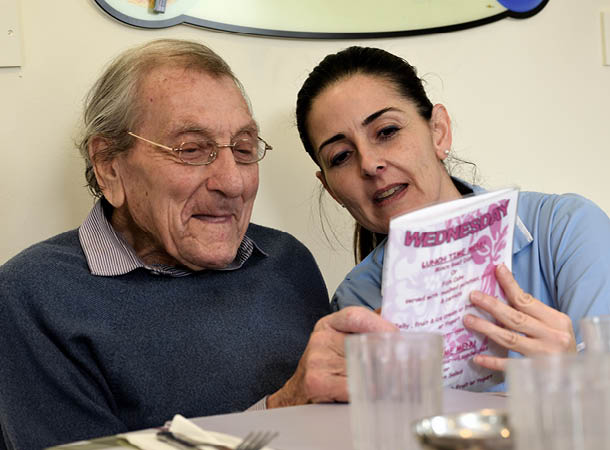 Carer helping elderly care home resident at mealtimes