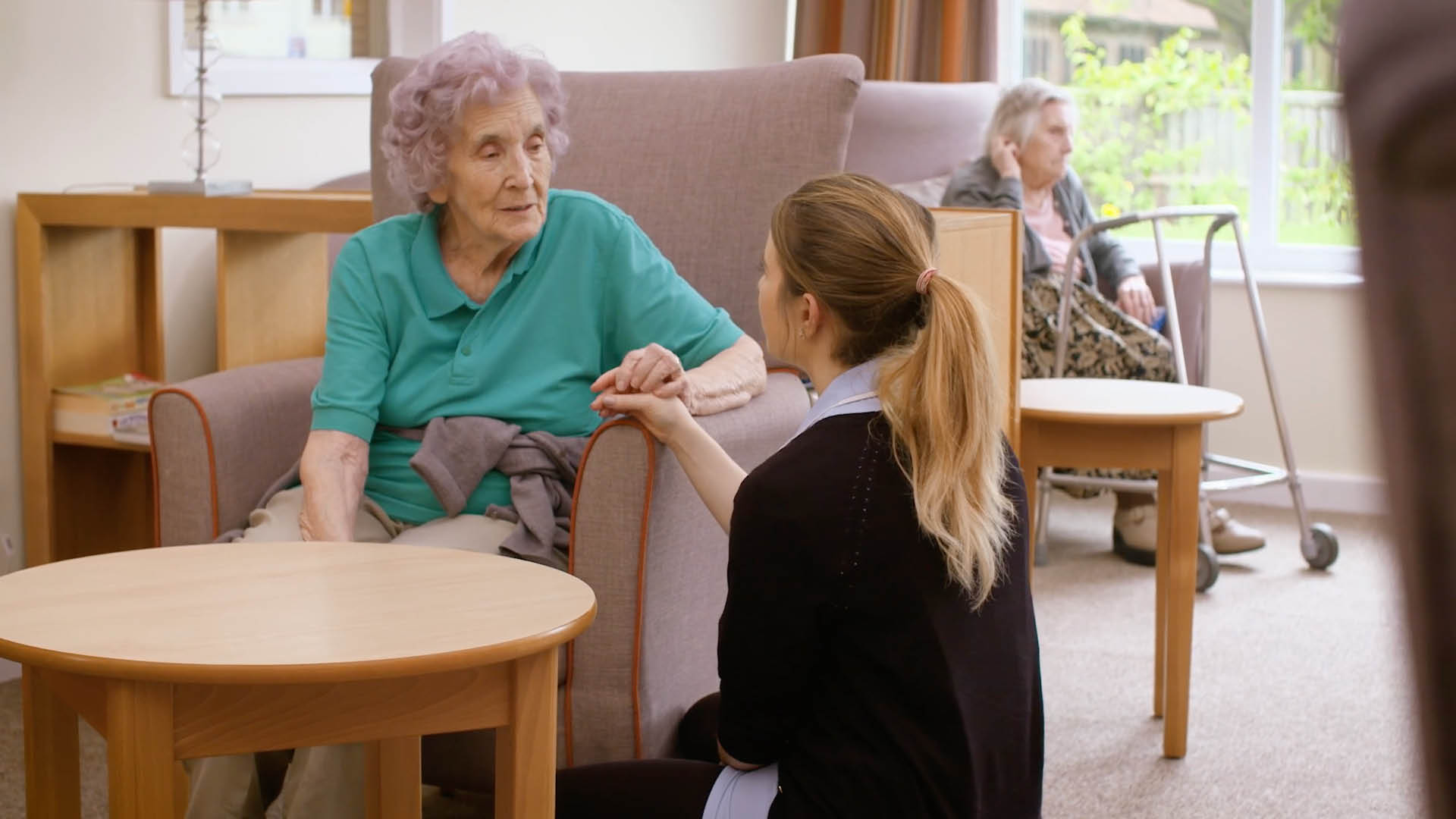 Cambridge care home young care assistant holding hands and talking to older person